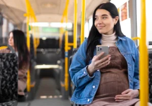 mulher gestante com celular na mão sentada dentro do ônibus